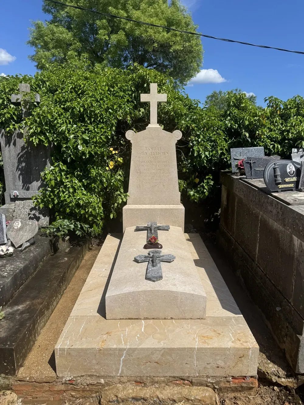 Monument funéraire rénové en pierre claire surmonté d'une croix chrétienne.