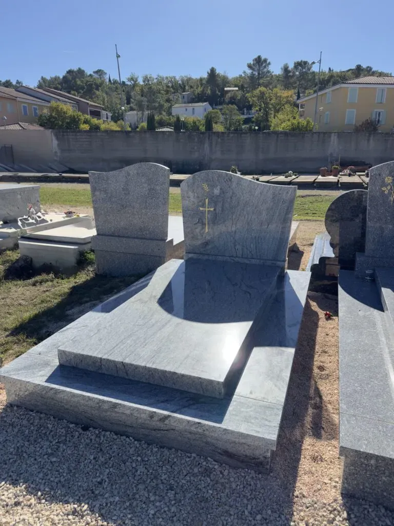 Monument funéraire double en granit clair gravé d'une croix dorée.