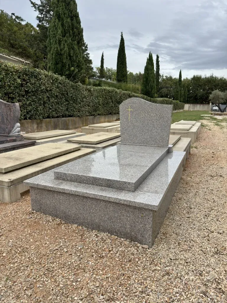 Pierre tombale sobre en granit gris érigée dans une allée du cimetière.